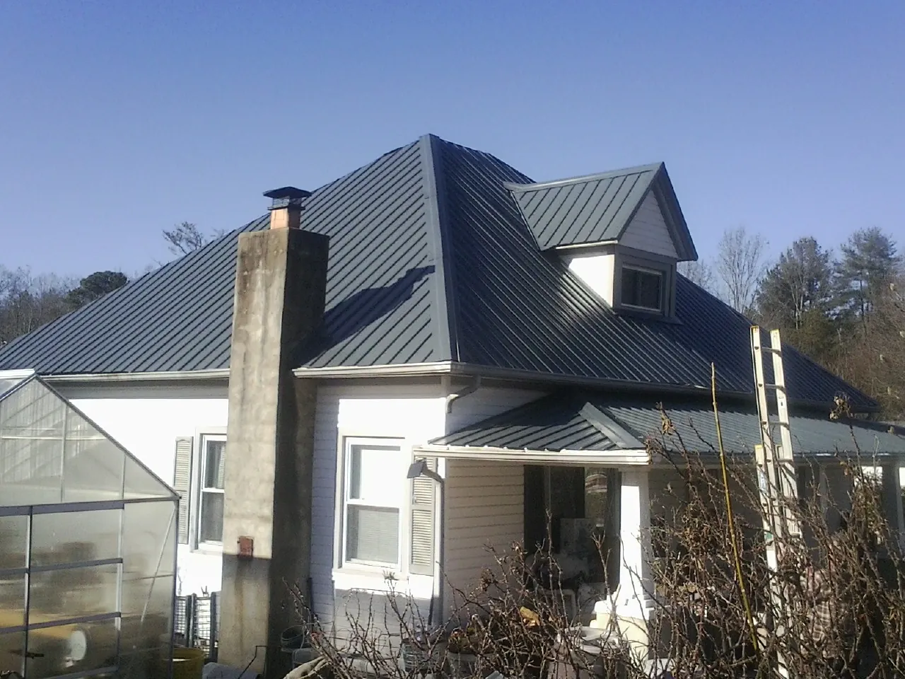 Dark blue standing seam metal roof on a white farmhouse with dormer in Thief River Falls