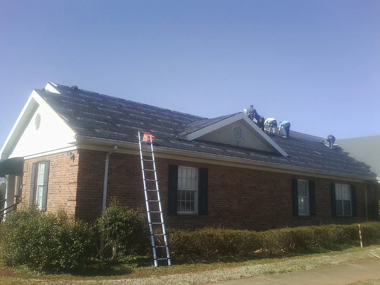 Crew tearing shingles off a brick ranch roof with a ladder set — Emergency Roof Repair work by our crew in Thief River Falls