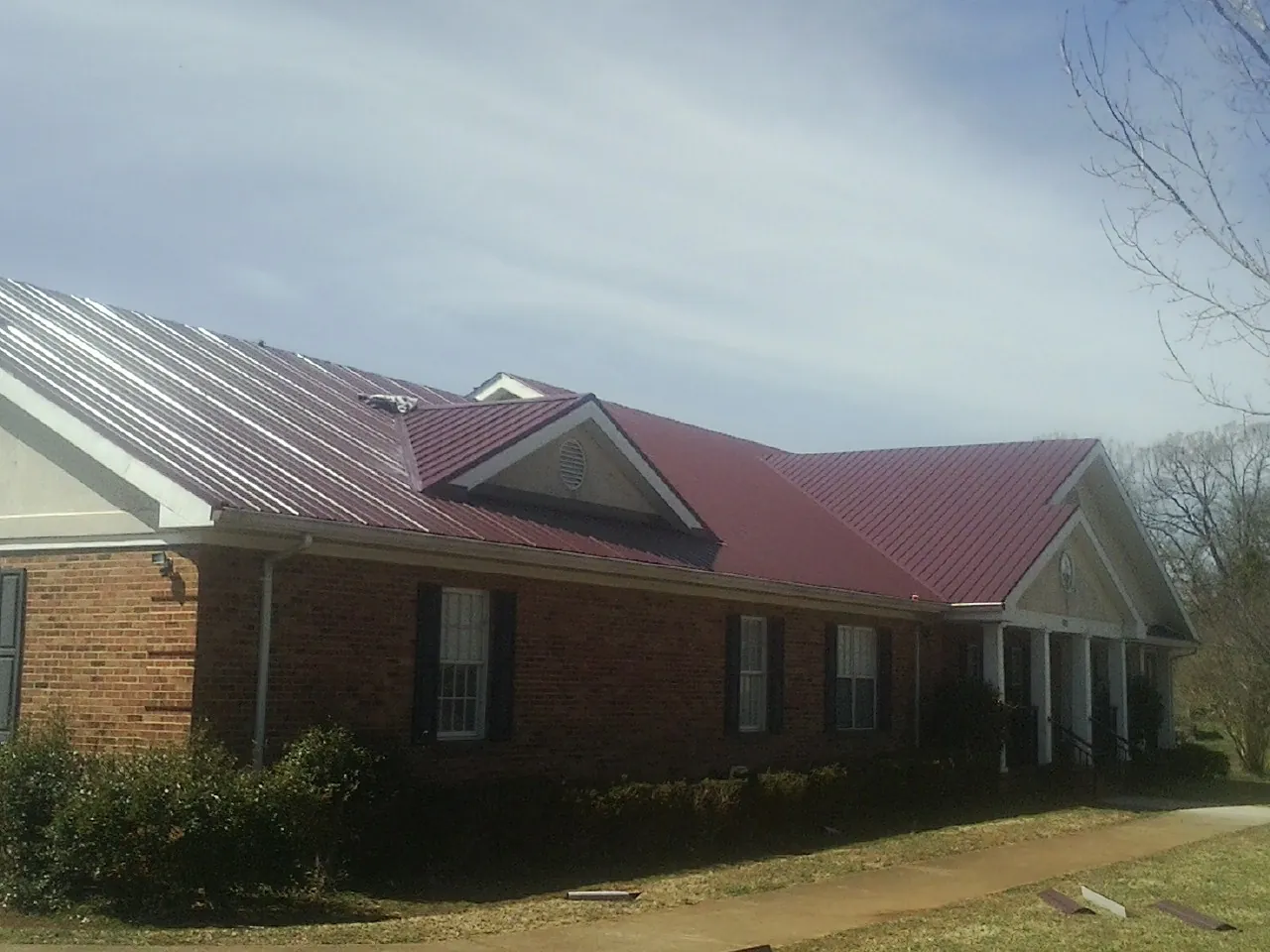 Red metal roof with gabled entries on a long brick building, from a Hail Damage Roof Repair job in Thief River Falls