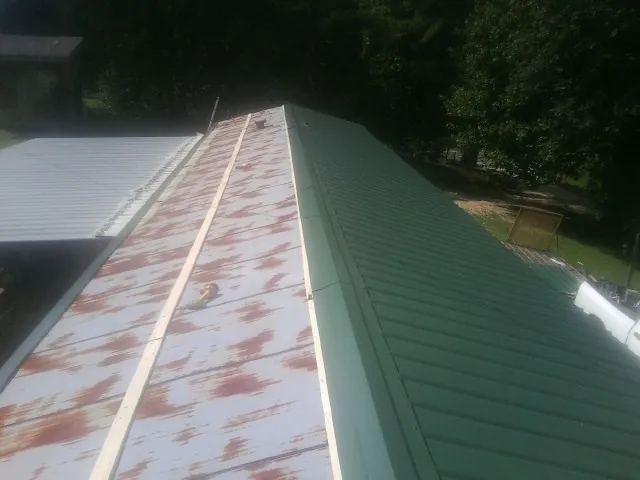 Old rusted panels beside newly installed green metal roofing — Wind Damage Roof Repair by Roofing Brothers in Thief River Falls