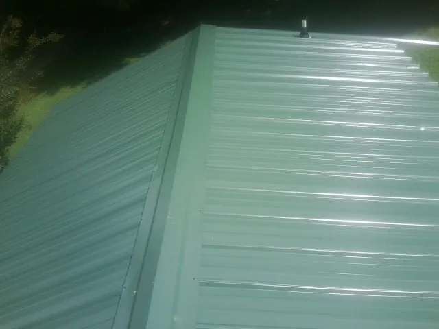 New green metal panels meeting at the ridge of a roof — Flat Roof Repair work by our crew in Thief River Falls