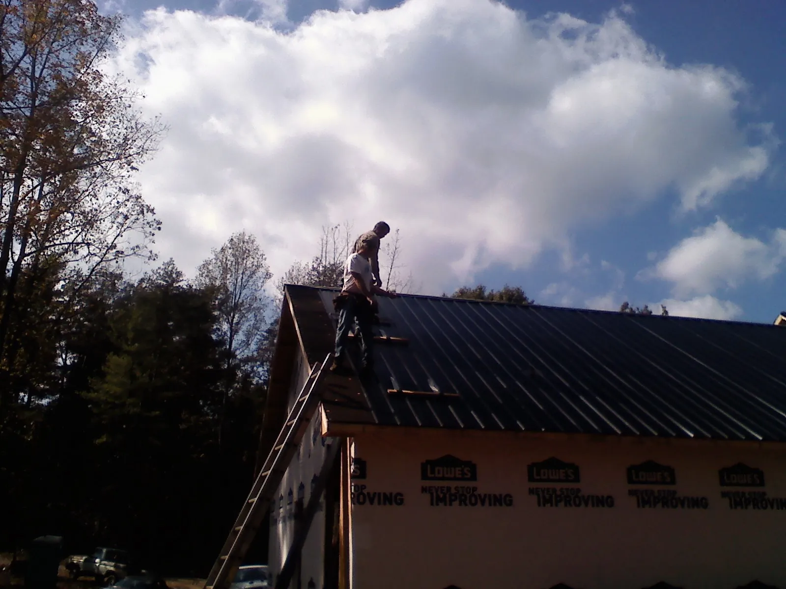 Roofer fastening dark metal panels high against a cloudy sky, from a Roof Inspection job in Thief River Falls