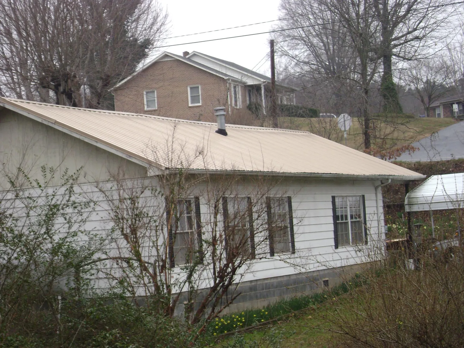 Tan metal roof on a white sided house set into a hillside — Commercial Roofing by Roofing Brothers in Thief River Falls