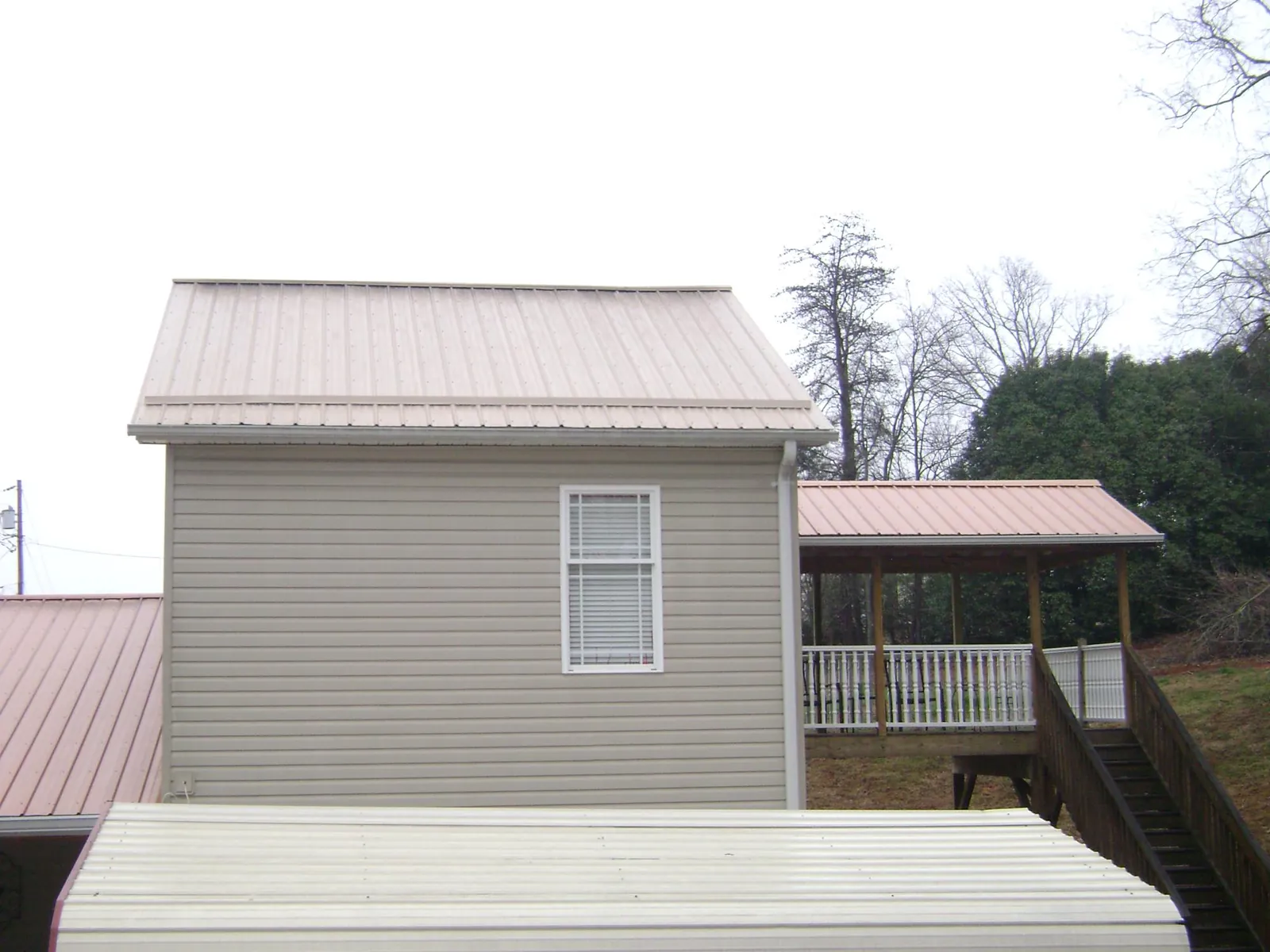 Tan metal roofs on a two story addition and attached porch, from a Roof Replacement job in Thief River Falls